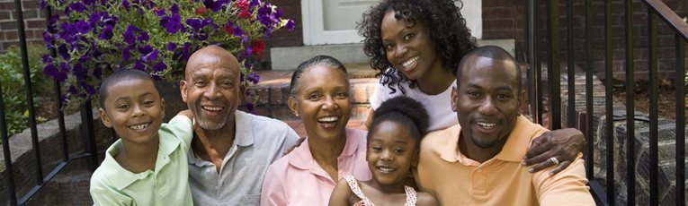 Multi-generational African-American family sitting on front steps of a home smiling at the camera.